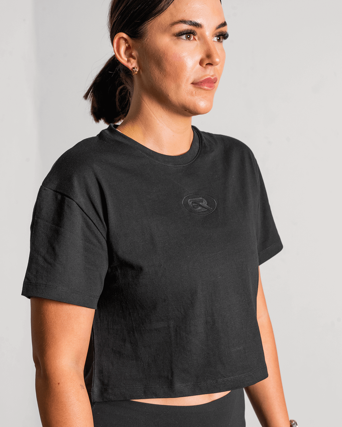 Woman wearing a black crop top with a logo on a plain background