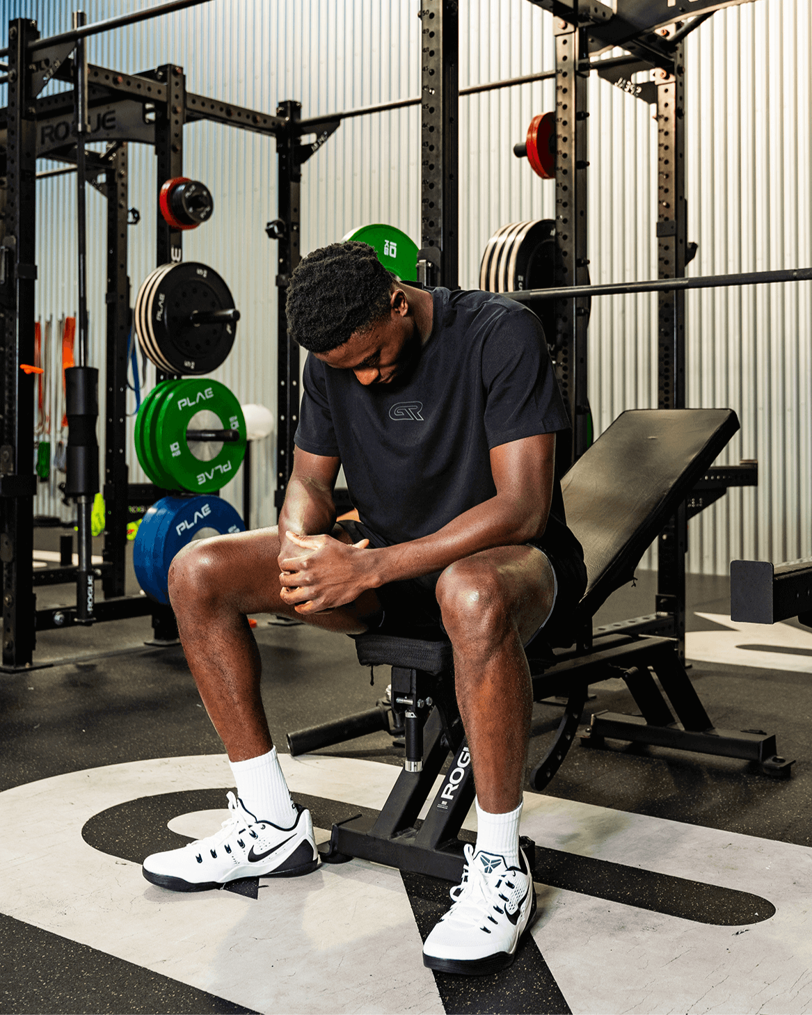 Man sitting on a weight bench in a gym setting with fitness equipment around
